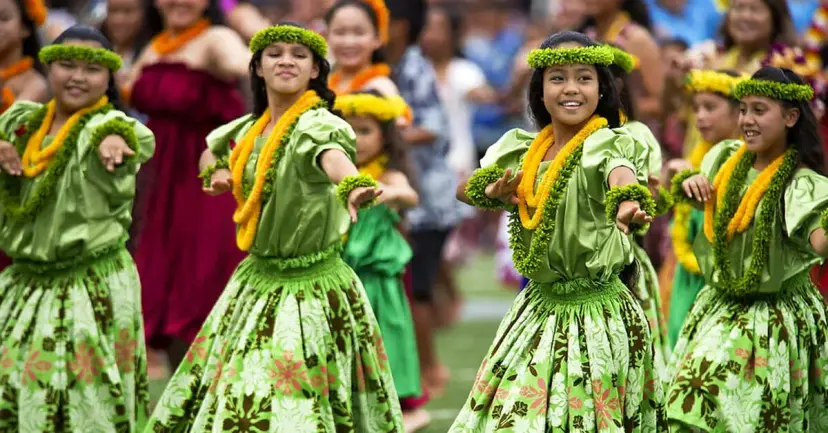 Young hula dancers in green dresses, yellow leis and leaf headpieces performing at an outdoor festival.