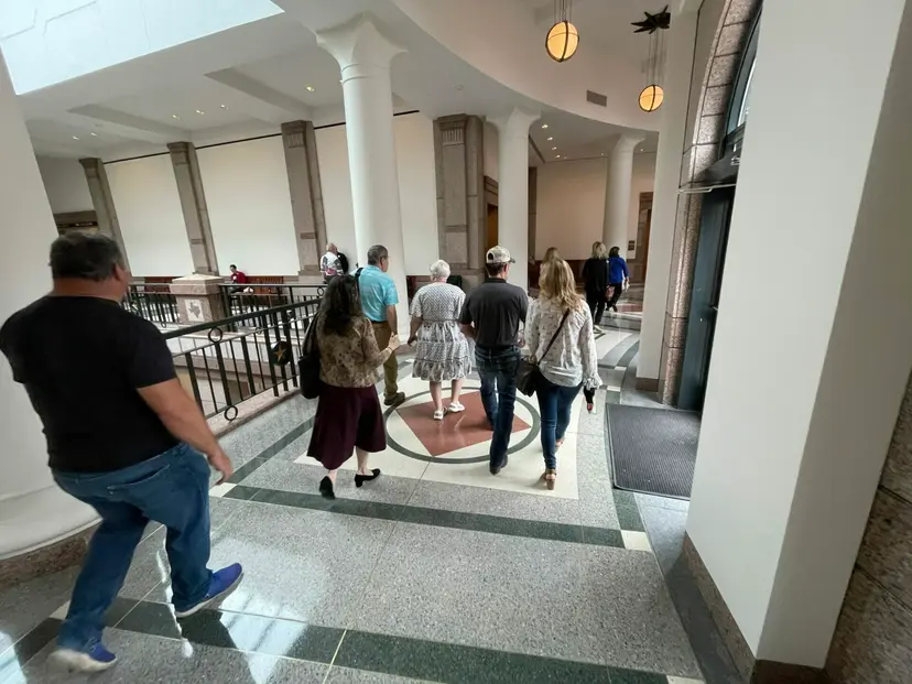 Supporters walk through a bright hallway with white columns in the Texas Capitol extension.