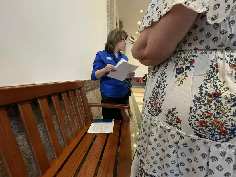 A woman in a blue TNM shirt reviews papers beside a wooden bench in a Capitol hallway.