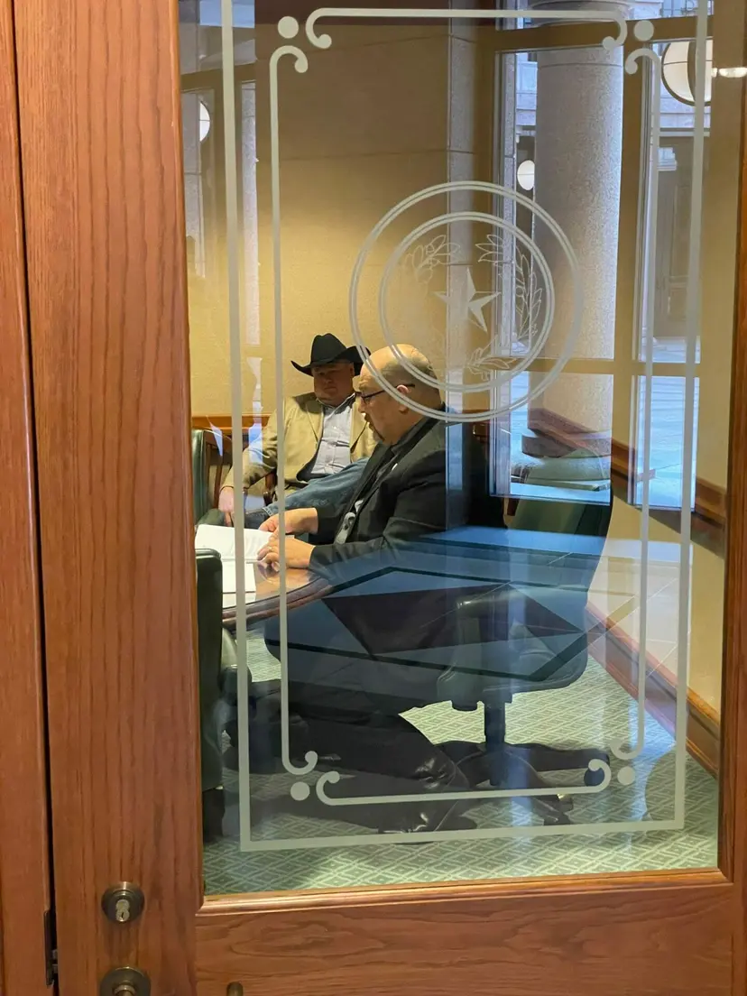 Through an etched glass door with the Texas seal, a staff member sits at a desk.