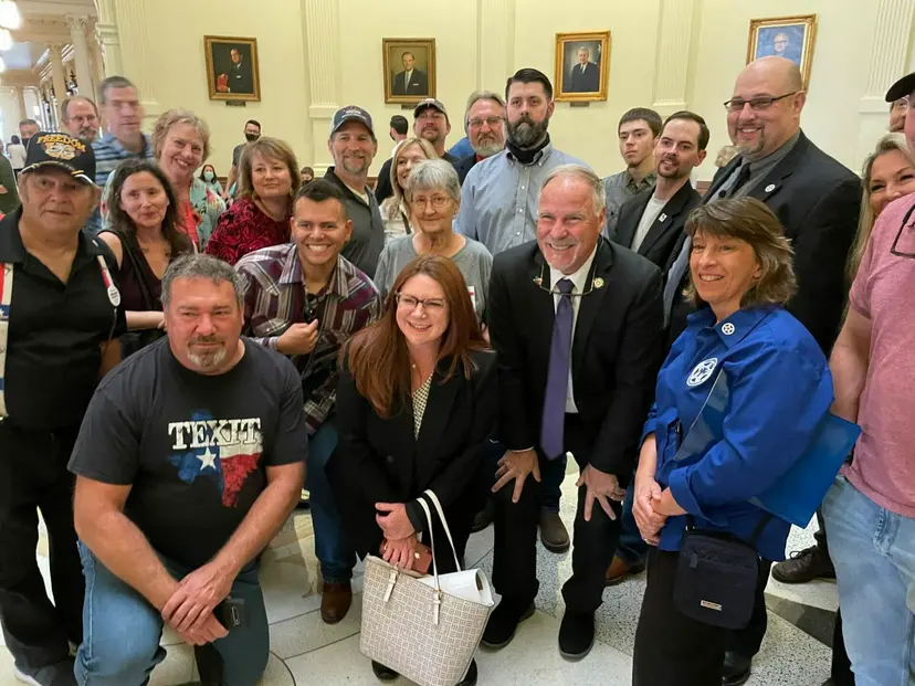A close group photo of smiling supporters in the Capitol, one wearing a TEXIT shirt.