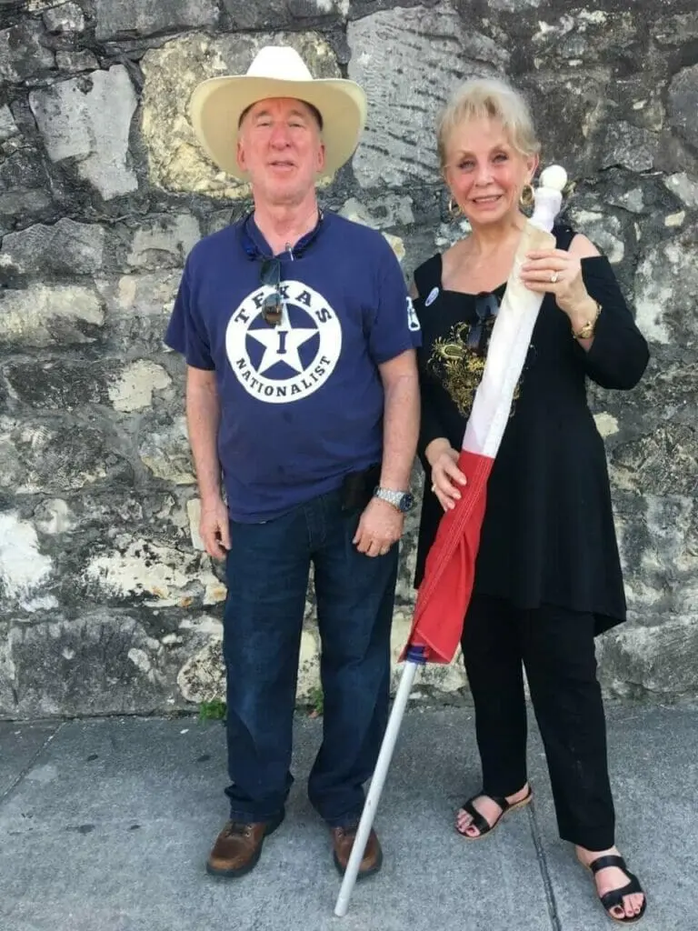 A man in a cowboy hat and Texas Nationalist shirt stands with a woman holding a Texas flag.