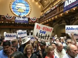Crowd holding Abbott campaign signs, including a handmade 'Re-elect Gov Abbott' sign, inside a domed hall.