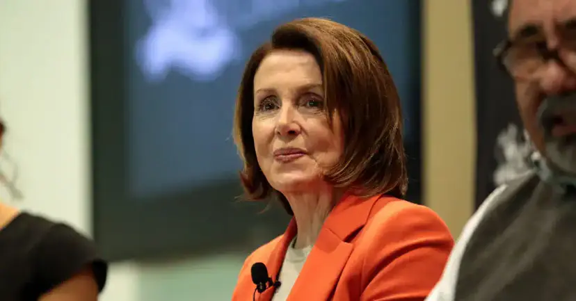 A woman in an orange blazer wearing a lapel microphone, seated at an indoor event.