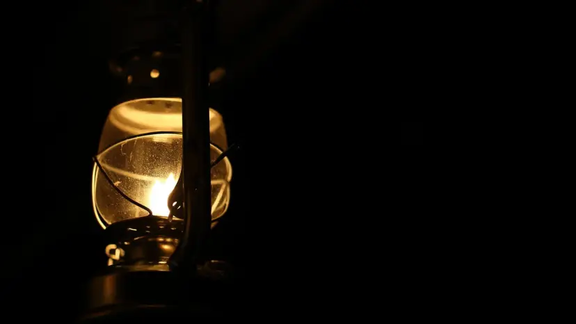 A glowing oil lantern hanging in total darkness, its small flame the only light in the frame.