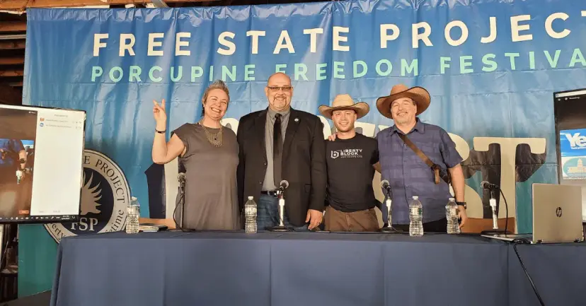 Four panelists pose at a table in front of a Free State Project Porcupine Freedom Festival banner.