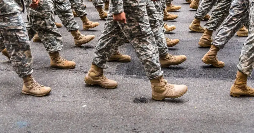 Soldiers in camouflage uniforms and tan boots marching in step on pavement.