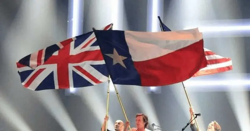 British Union Jack and Texas flag waved together under stage lights, with an American flag behind them.