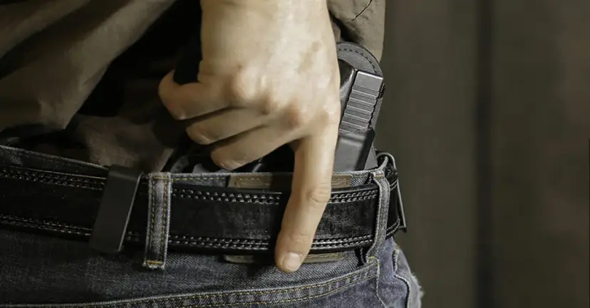 Hand drawing a handgun from a concealed holster tucked inside a belt and jeans.