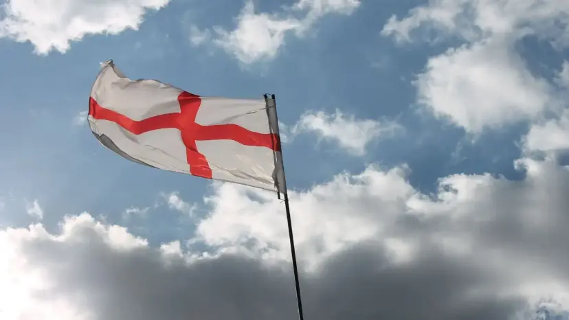 The red and white St. George's Cross flag of England flies against a blue sky with white clouds.