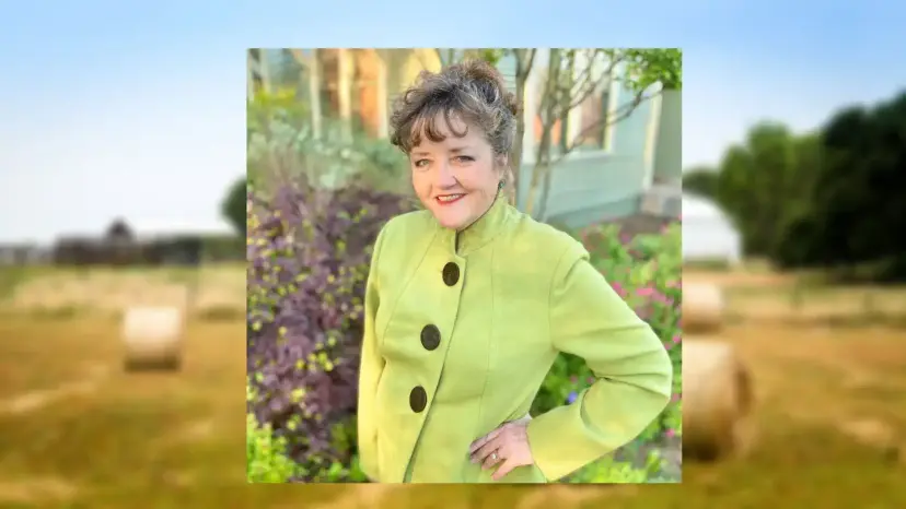 Sheila Hemphill in a lime green jacket smiling in a flower garden, framed over a blurred hay field.