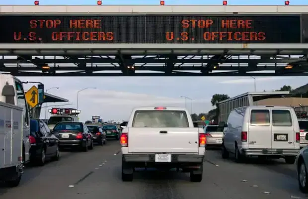Traffic lines up under an electronic sign reading 'Stop Here U.S. Officers' at a federal highway checkpoint.