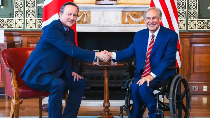 Governor Greg Abbott shaking hands with a British official in a formal room before British and American flags.