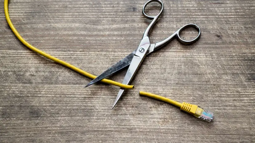 Scissors cutting a yellow ethernet cable on a wooden table.