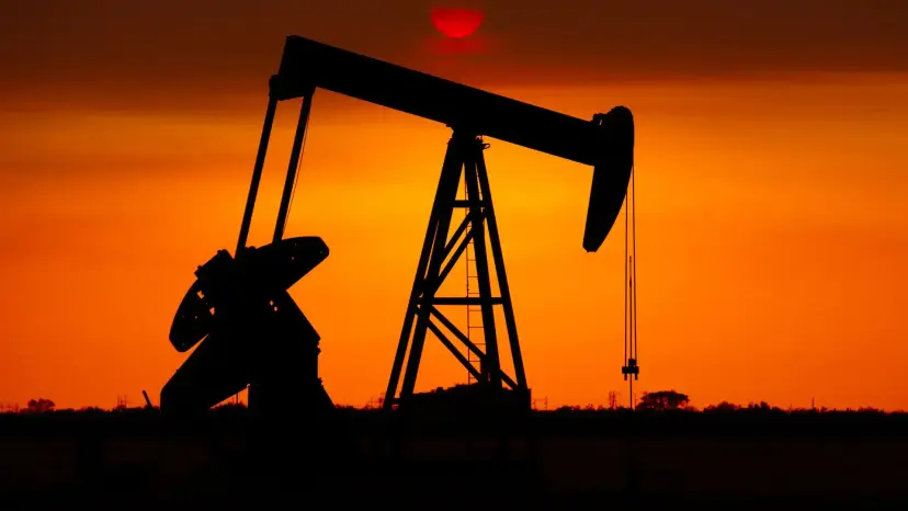 Silhouette of a single oil pump jack against a deep orange sunset.