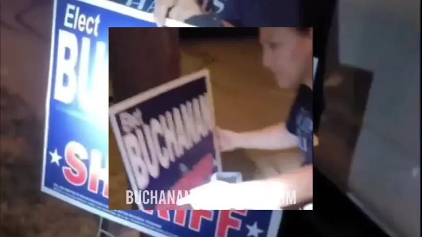 A blurry video still of a person grabbing a 'Buchanan for Sheriff' campaign yard sign.