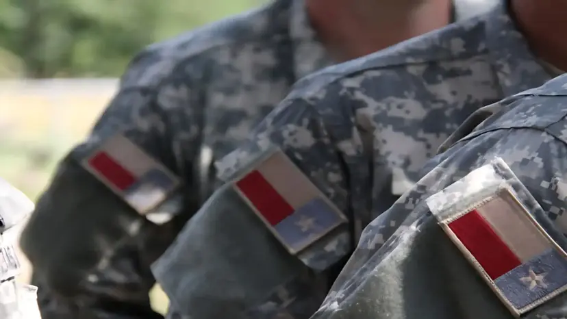 Close-up of soldiers' camouflage uniform sleeves bearing Texas flag patches.