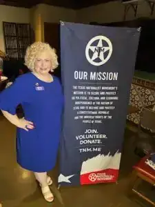 A woman in a blue dress standing beside a Texas Nationalist Movement banner titled 'Our Mission.'