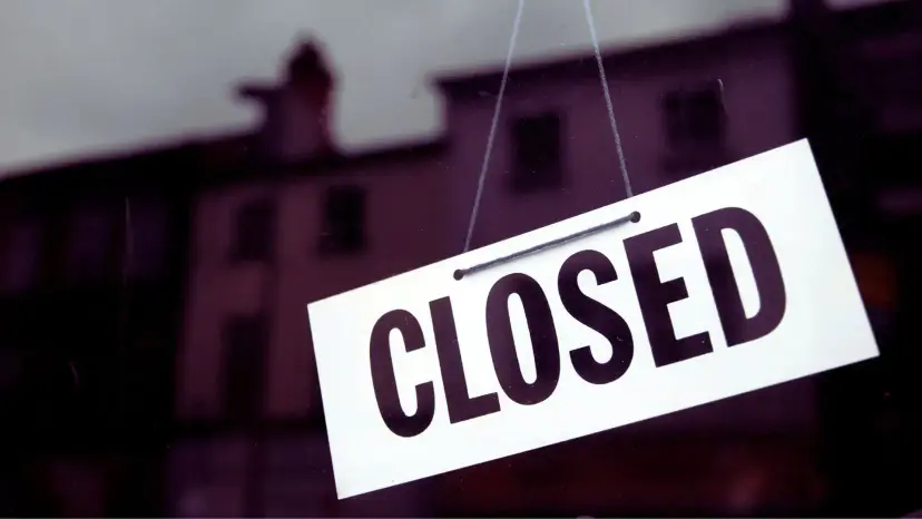 A white 'Closed' sign hanging in a window in front of a dark building.