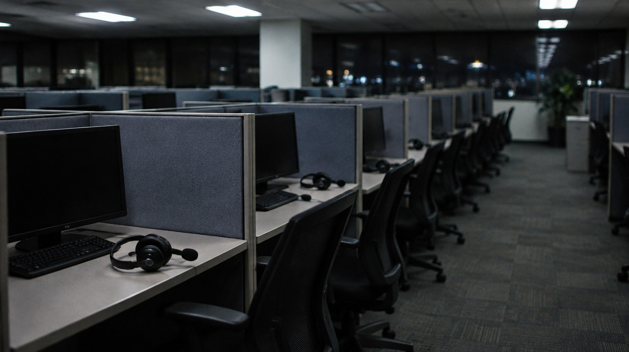 An empty telephone survey call center at night, with headsets resting on the desks.