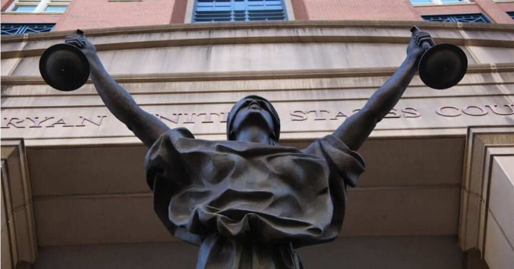 Bronze statue of a blindfolded figure holding up scales in front of a federal courthouse.