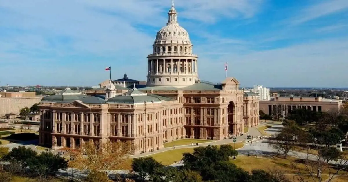 Aerial view of the Texas Capitol in Austin under a blue sky with scattered clouds.