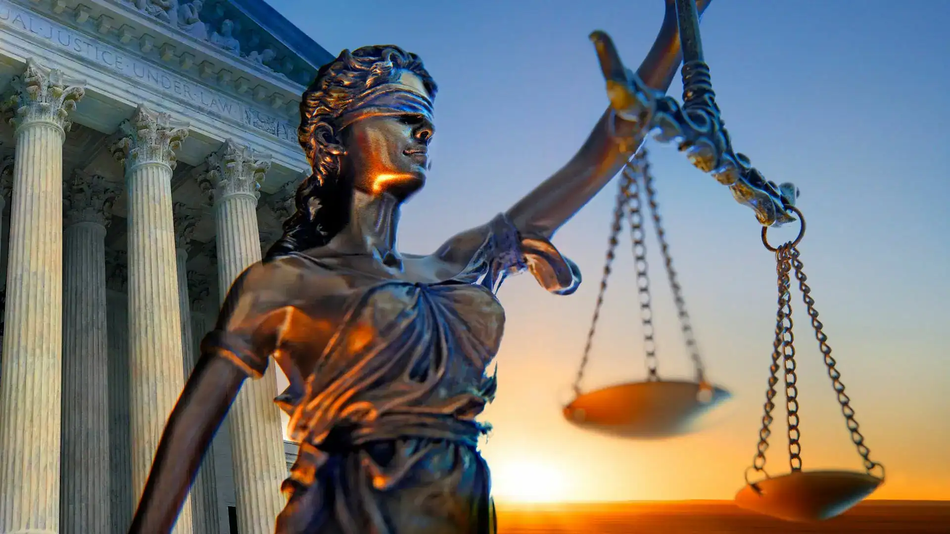 A bronze statue of blindfolded Lady Justice holding scales in front of a columned courthouse at sunset.
