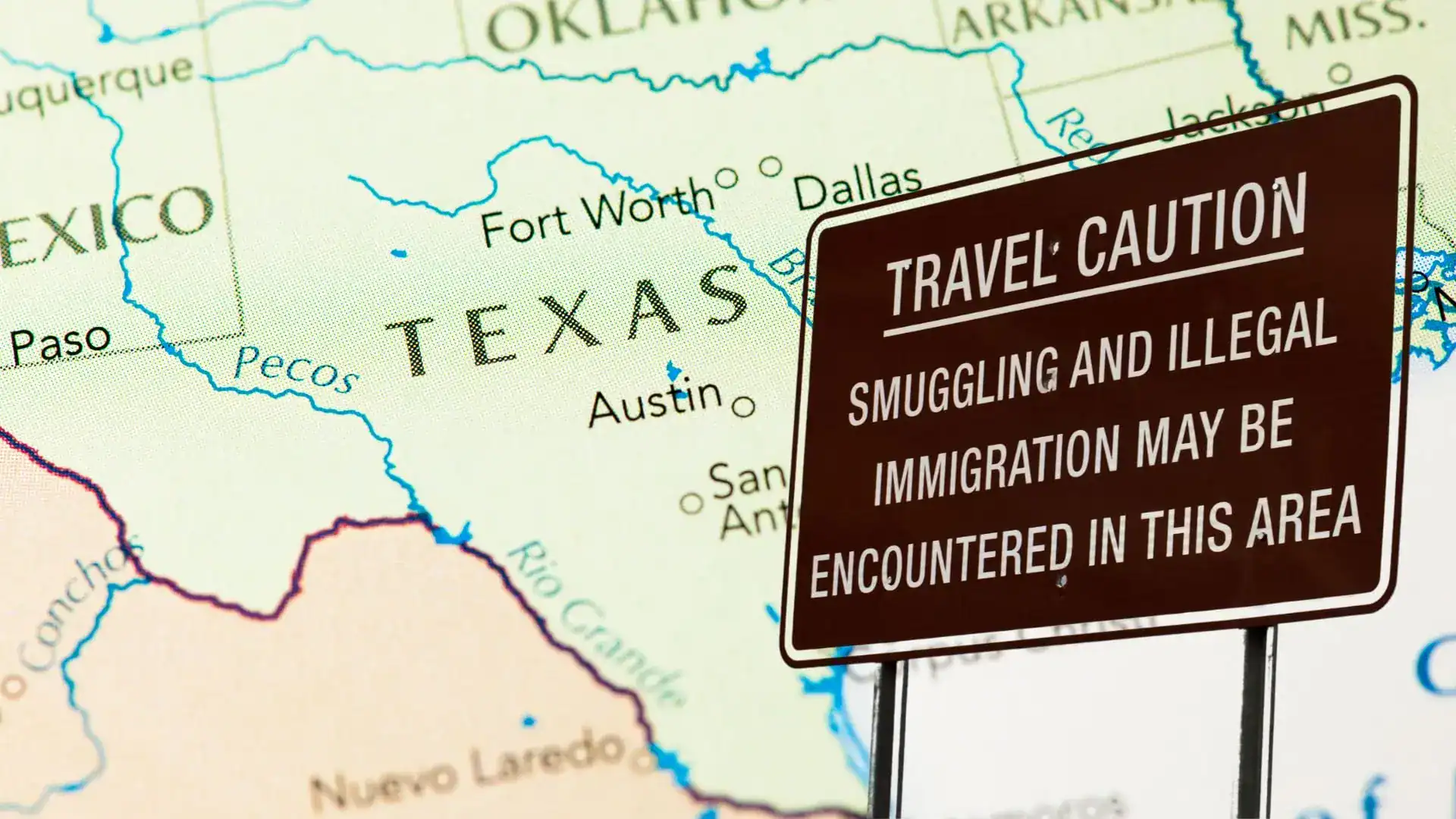 A brown sign reading 'Travel Caution: Smuggling and illegal immigration may be encountered in this area' over a Texas map.