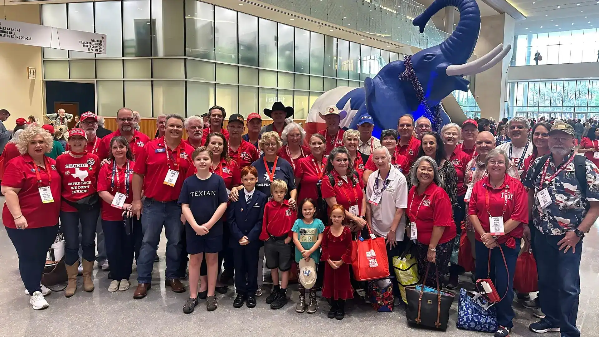 A large group in red shirts poses in a convention center lobby in front of a giant blue elephant statue.