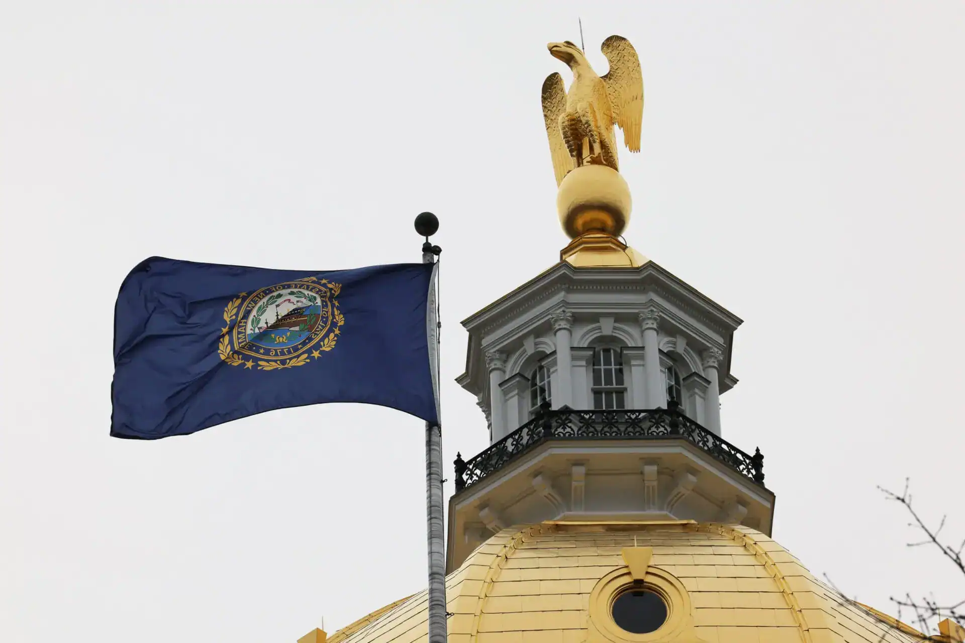 The New Hampshire state flag flies beside the gold eagle atop the State House dome in Concord.
