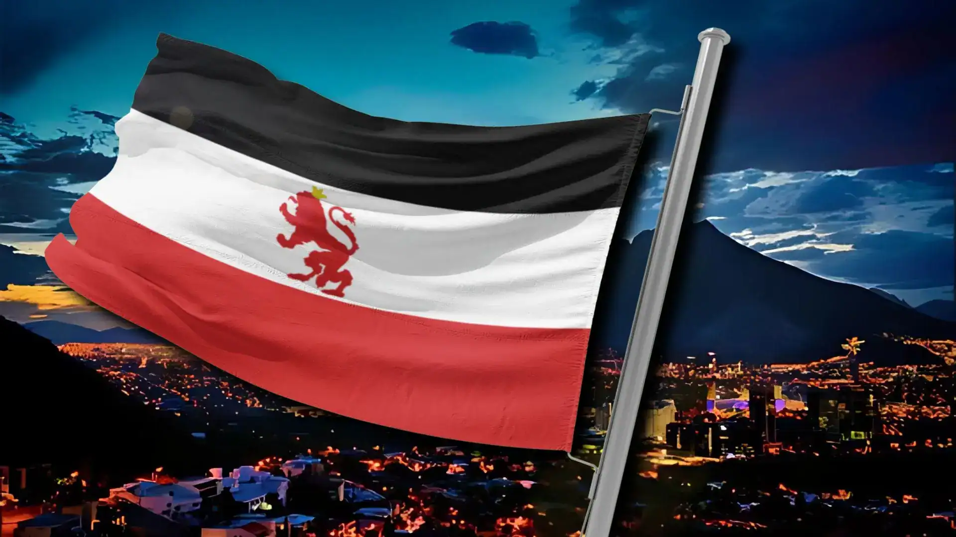 A striped flag with a red lion on a white band flying over a city at night below mountains.