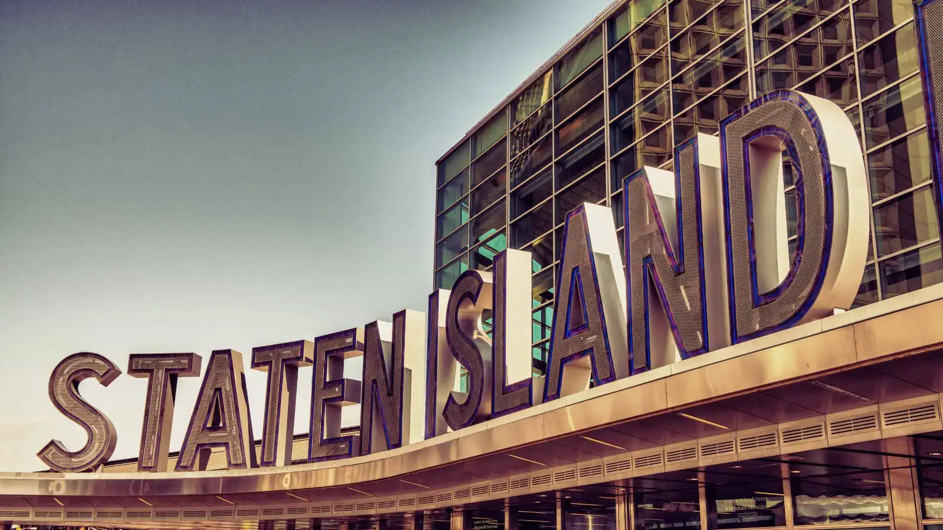 Large 'Staten Island' letters stand atop a glass terminal building against a clear sky.