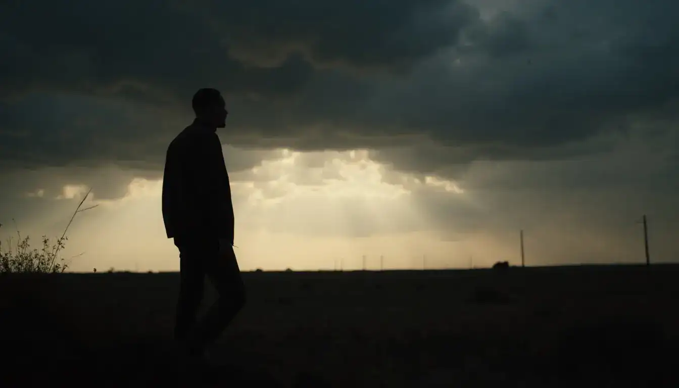 Silhouette of a man walking across open prairie under dark storm clouds with light breaking on the horizon.