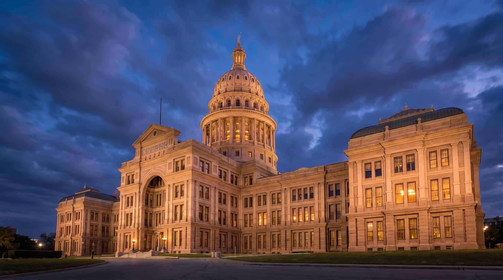 The Texas State Capitol in Austin at blue hour, its pink granite dome and facade lit against a deep blue evening sky