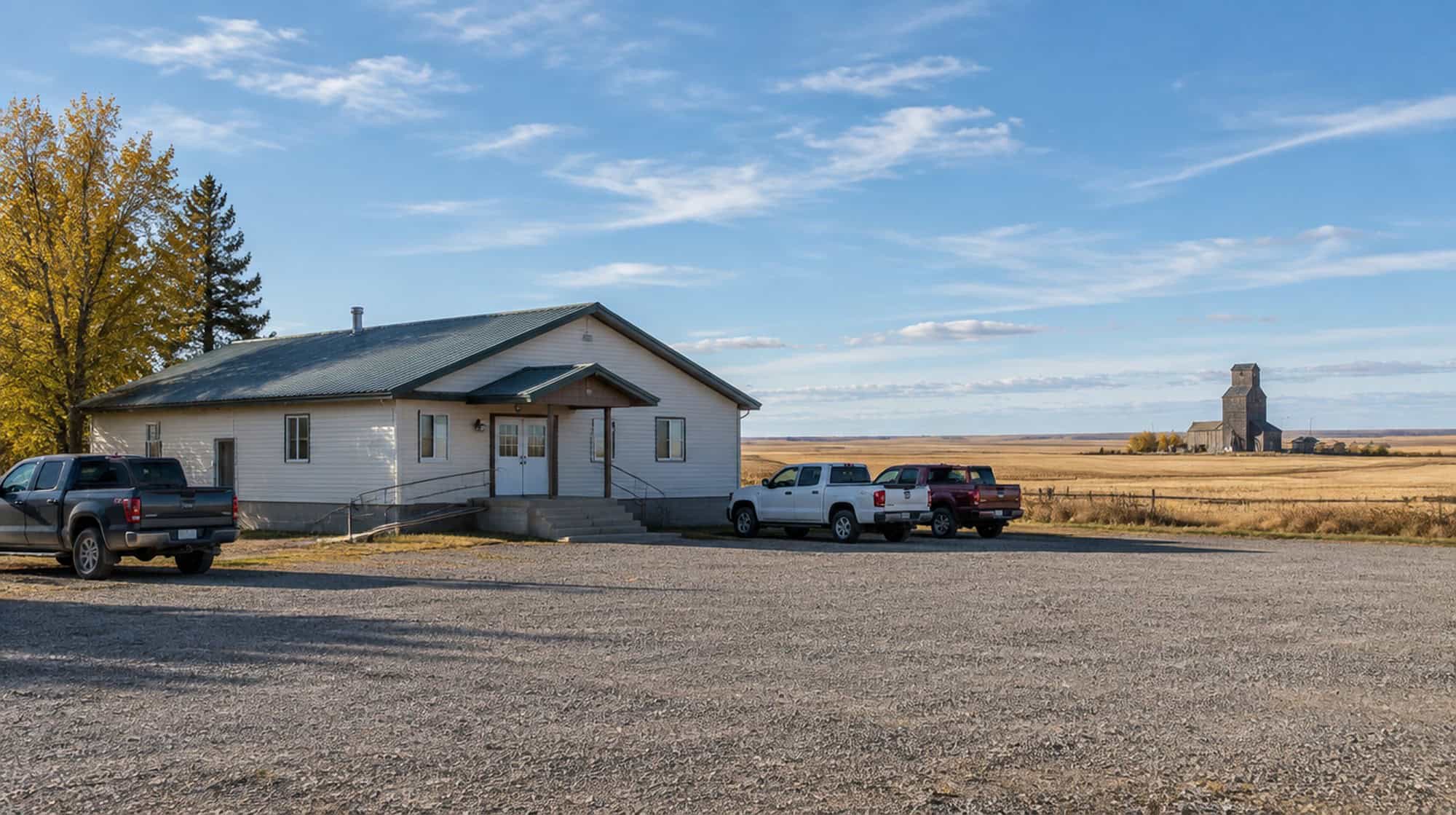 A rural community hall on the Alberta prairie with a grain elevator on the horizon on an autumn morning.